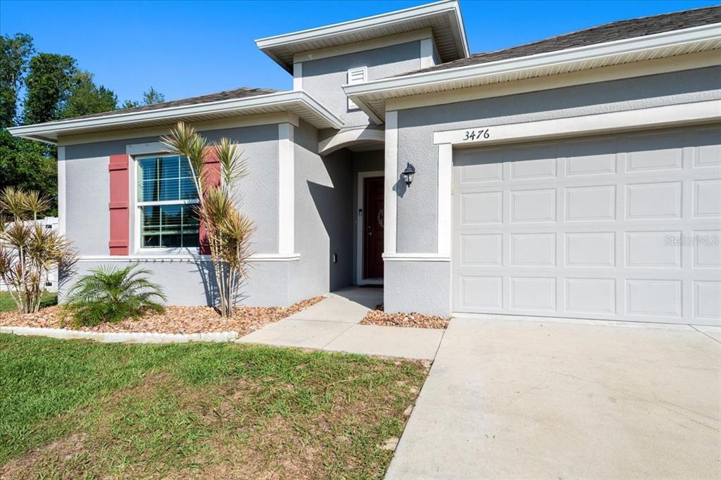 A gray single-story house features a red front door, a garage, and a landscaped yard — 3476 BREWSTER ROAD, NORTH PORT, FL