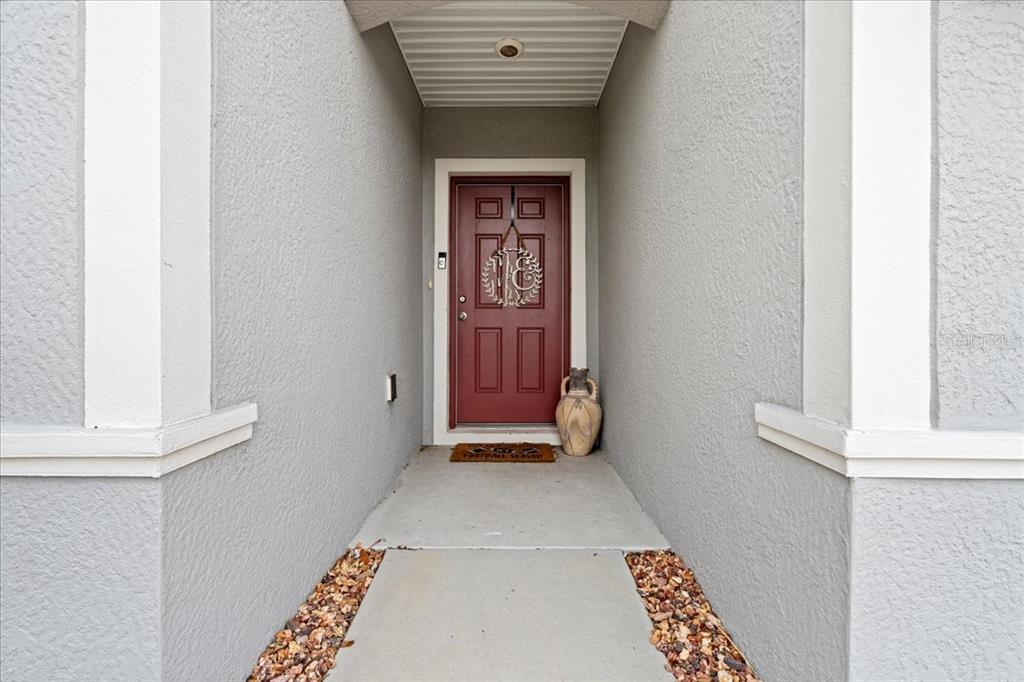 A covered entryway features a red front door with a wreath and a concrete walkway — 3476 BREWSTER ROAD, NORTH PORT, FL