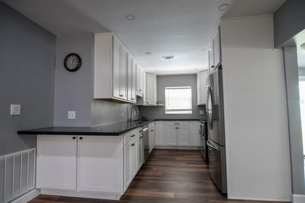 A kitchen features white cabinets, black countertops, stainless steel appliances, and dark wood-look flooring — 103 DELLWOOD DRIVE, KISSIMMEE, FL