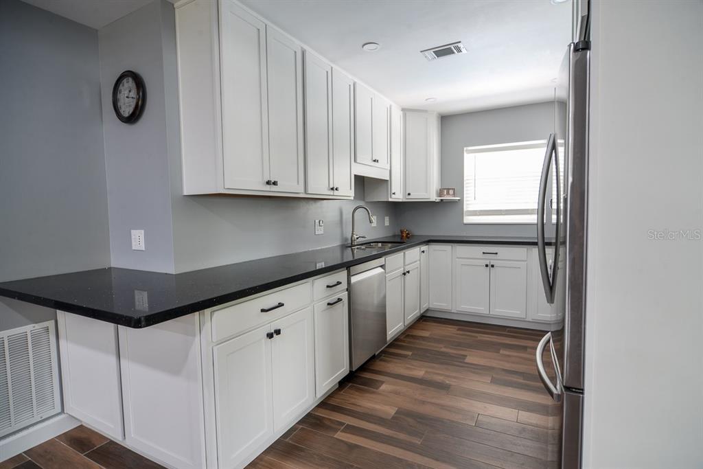 A kitchen features white cabinets, black countertops, stainless steel appliances, and wood-look flooring — 103 DELLWOOD DRIVE, KISSIMMEE, FL