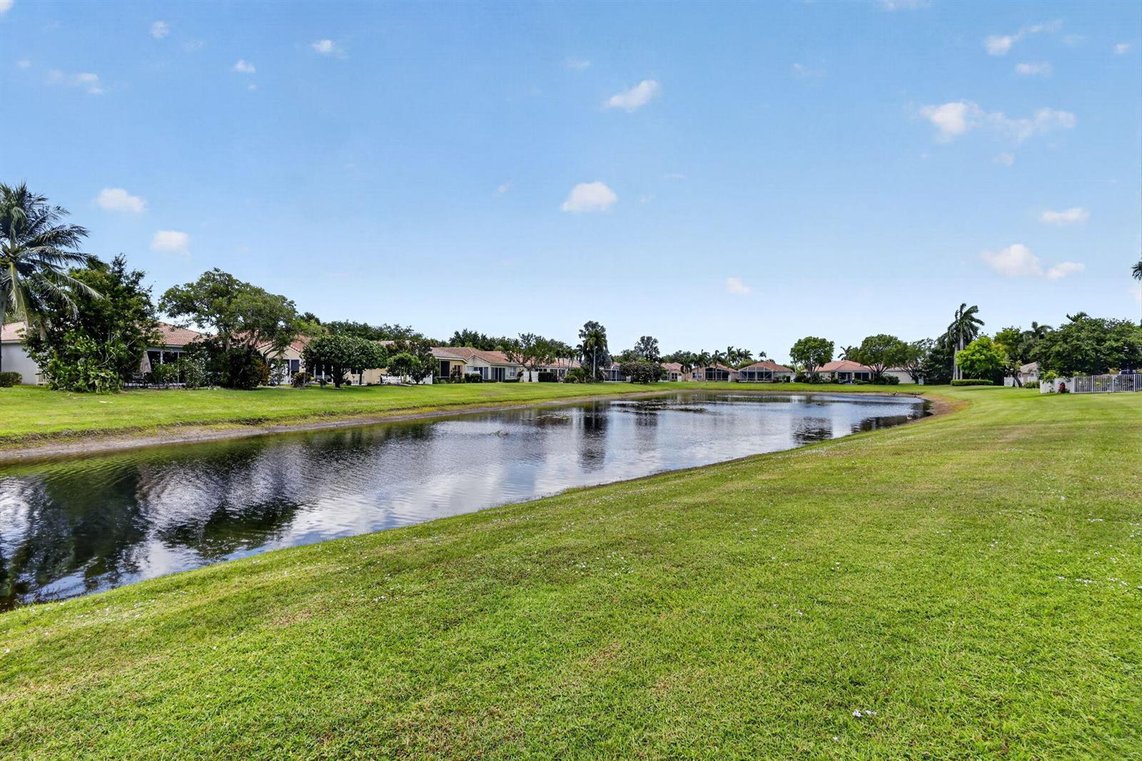 A grassy lawn slopes down to a pond with residential houses in the background — 12530 Vía Valenza, Boynton Beach FL 33436, BOYNTON BEACH, FL