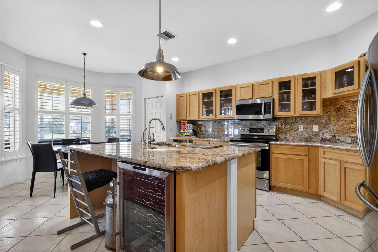 A kitchen features light wood cabinets, granite countertops, a center island, and tile flooring — 12530 Vía Valenza, Boynton Beach FL 33436, BOYNTON BEACH, FL