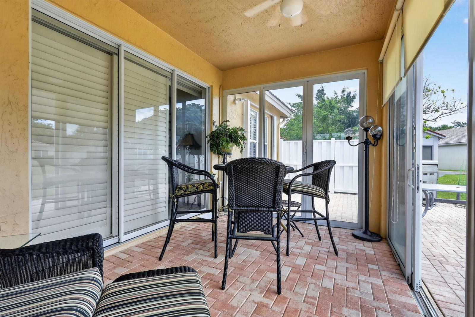 A covered patio features a brick floor, wicker furniture, and large glass sliding doors — 12530 Vía Valenza, Boynton Beach FL 33436, BOYNTON BEACH, FL