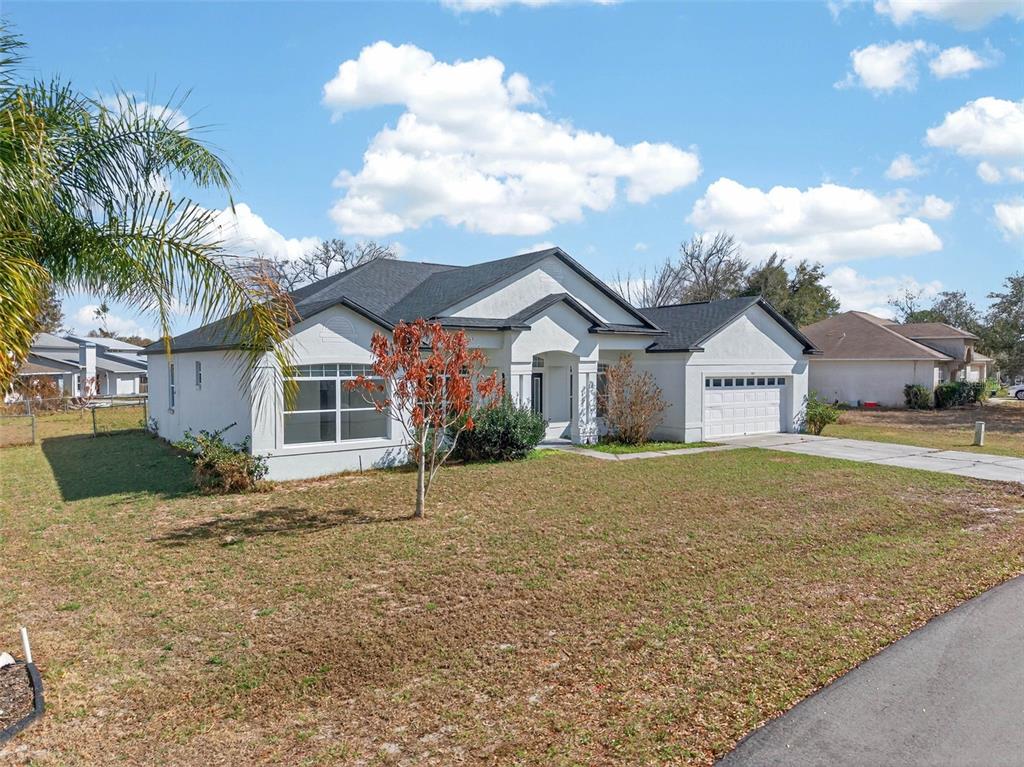 A single-story white stucco house with a dark shingled roof and a two-car garage — 183 LAKE THOMAS, WINTER HAVEN, FL