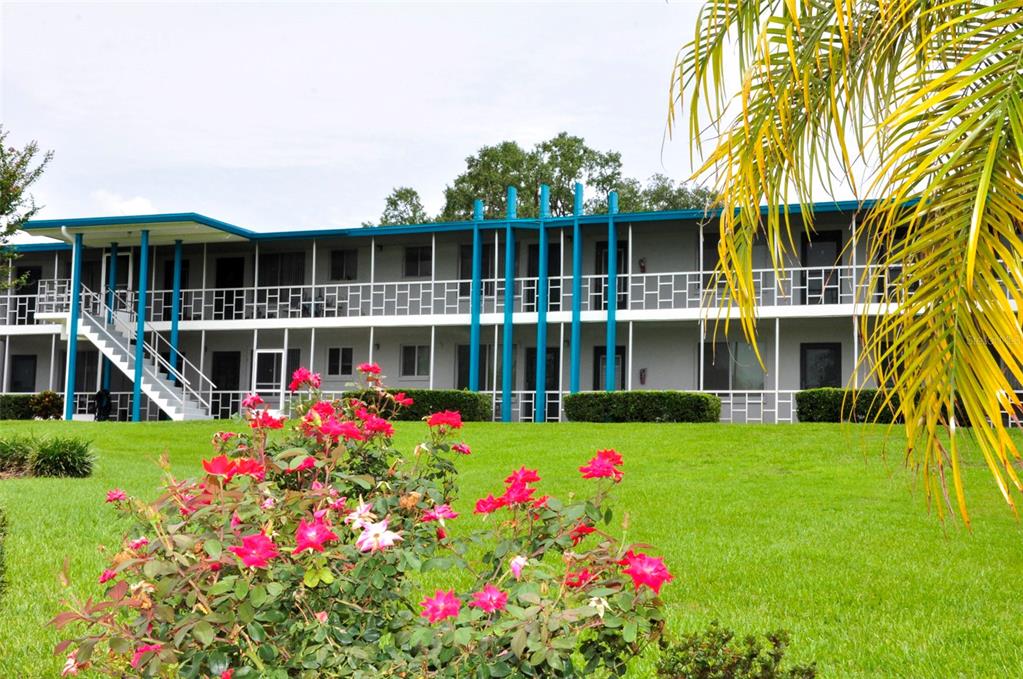 A two-story apartment building with a white balcony and blue accents sits behind rose bushes — 1600 W LAKE PARKER DRIVE UNIT B4, LAKELAND, FL