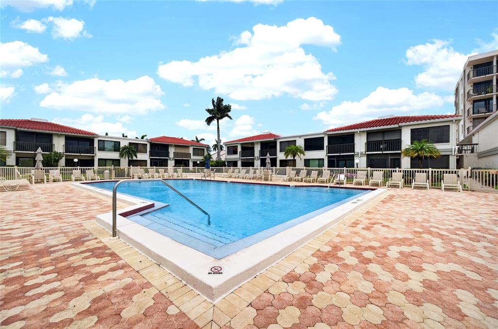 A rectangular swimming pool is surrounded by a brick paver deck and multi-story residential buildings — 6365 BAHIA DEL MAR BOULEVARD UNIT 106, ST PETERSBURG, FL