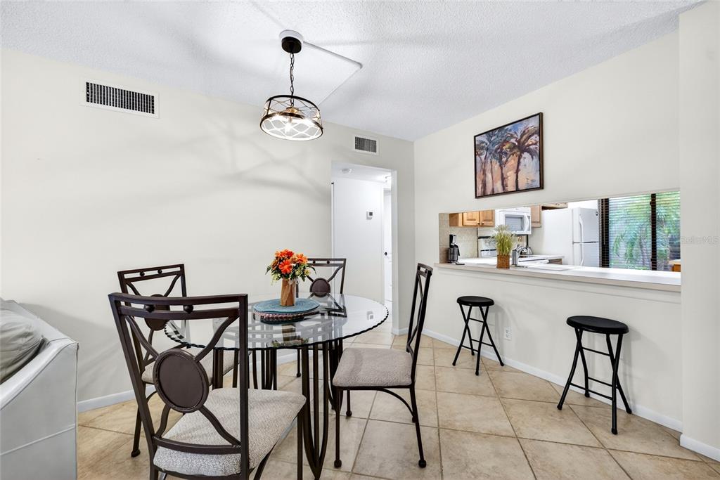 A dining area features a glass-topped table, metal chairs, bar stools, and a kitchen pass-through — 6365 BAHIA DEL MAR BOULEVARD UNIT 106, ST PETERSBURG, FL