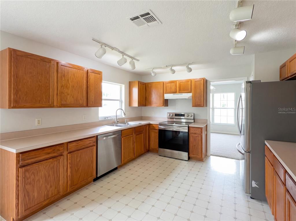 A kitchen features wood cabinets, stainless steel appliances, laminate countertops, and a tiled floor — 1021 DEKLEVA DRIVE, APOPKA, FL