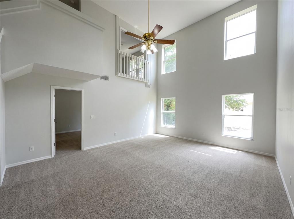 A high-ceilinged living room features beige carpeting, a ceiling fan, and an interior balcony — 1021 DEKLEVA DRIVE, APOPKA, FL