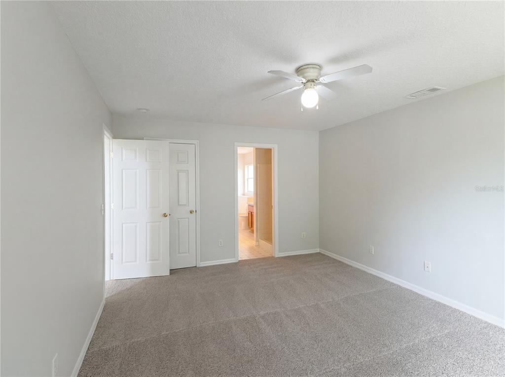 A bedroom with gray carpet, light gray walls, a ceiling fan, and an attached bathroom — 1021 DEKLEVA DRIVE, APOPKA, FL