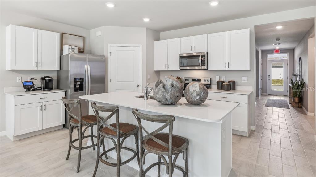 A modern kitchen features white cabinetry, stainless steel appliances, a central island, and tile flooring — 16332 NAVARRO COURT, PUNTA GORDA, FL