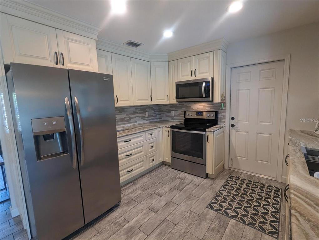 A kitchen features white cabinets, stainless steel appliances, a tiled backsplash, and wood-look floor tiles — 3070 GULF GATE DRIVE, SARASOTA, FL