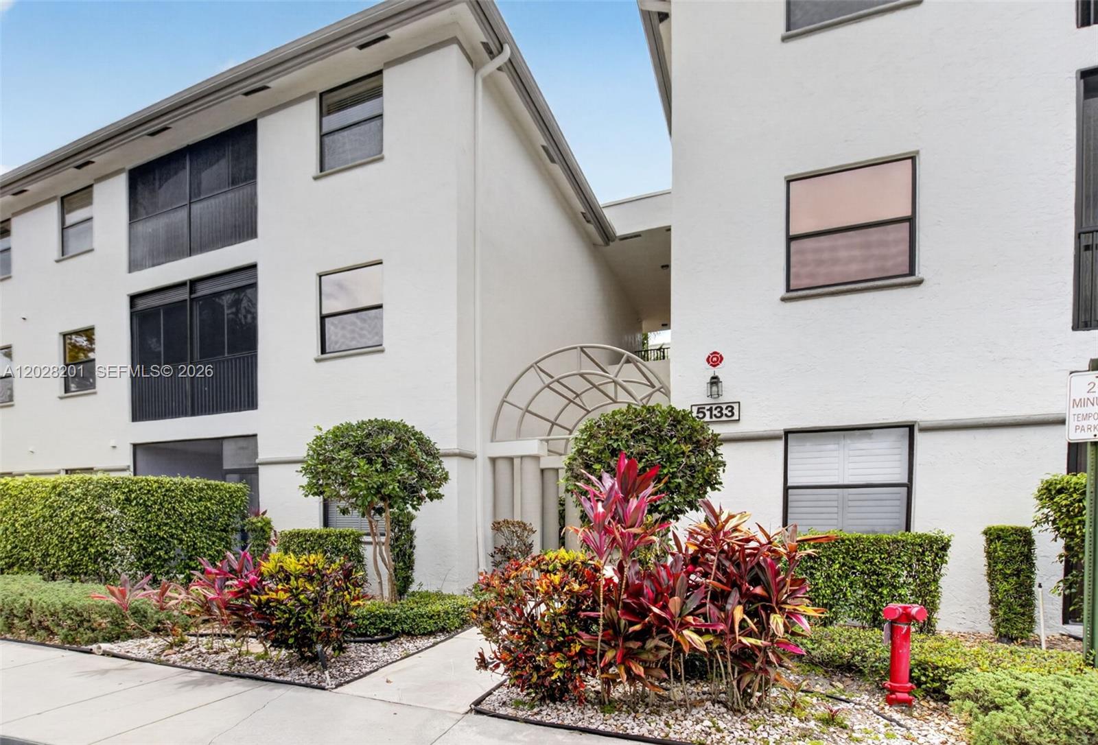 The exterior of a multi-story white apartment building features a landscaped entrance and walkway — 5133 Brisata Cir # L, Boynton Beach FL 33437, BOYNTON BEACH, FL