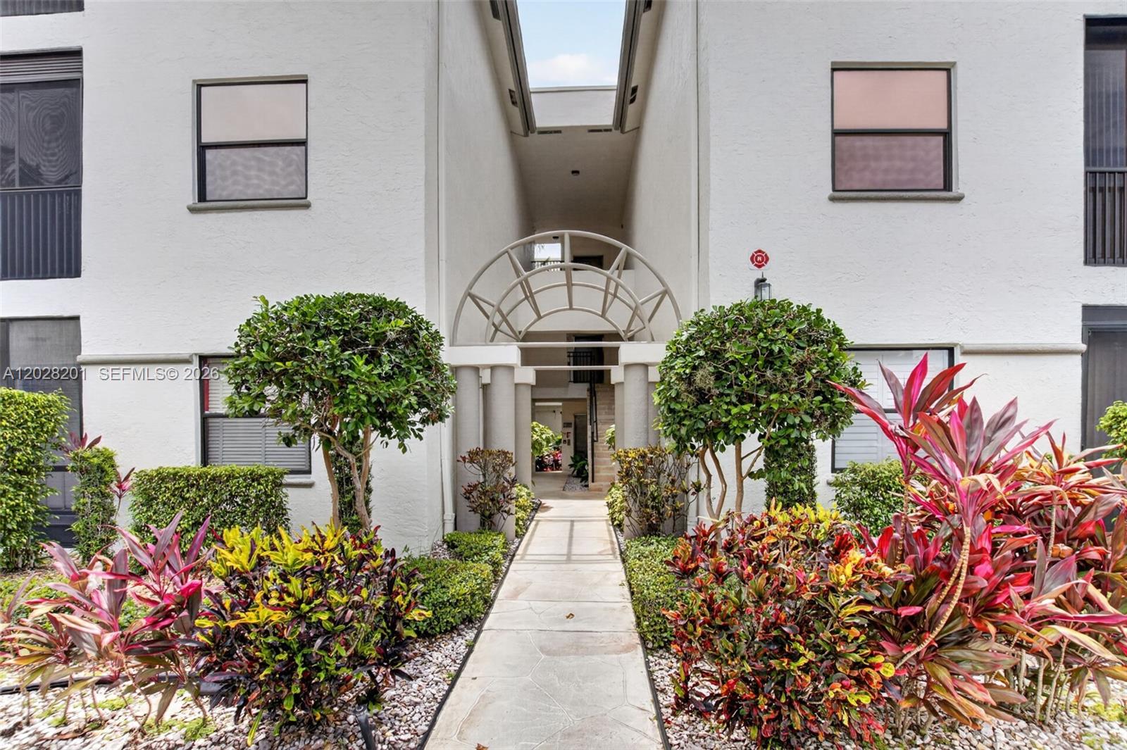 A paved walkway leads to the arched entryway of a two-story white stucco building — 5133 Brisata Cir # L, Boynton Beach FL 33437, BOYNTON BEACH, FL