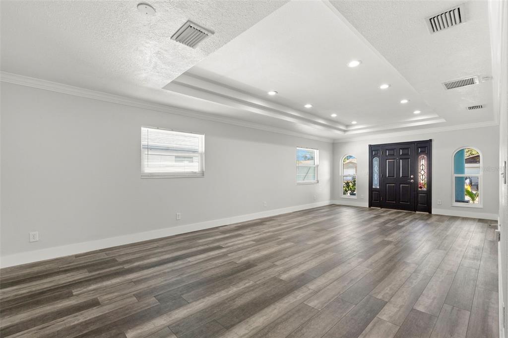 A spacious living room with gray wood-look flooring, a tray ceiling, and a black front door — 4510 68TH AVENUE N, PINELLAS PARK, FL