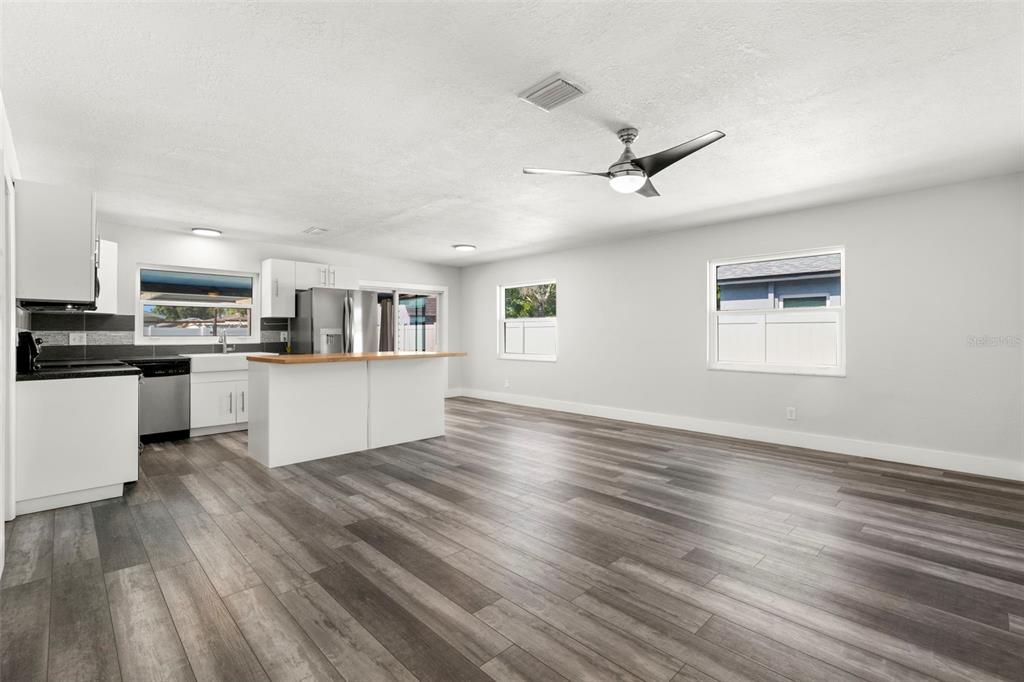 An open-concept kitchen and living area features white cabinetry, a wood-topped island, and gray flooring — 4510 68TH AVENUE N, PINELLAS PARK, FL