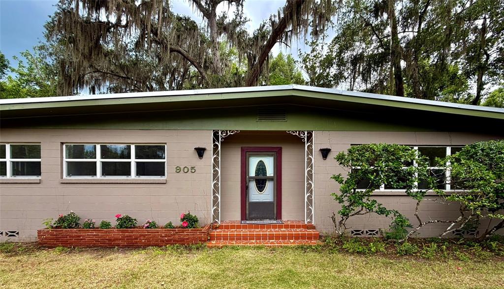 A single-story house with a flat roof, tan block walls, and a brick planter box — 905 NW 36TH AVENUE, GAINESVILLE, FL