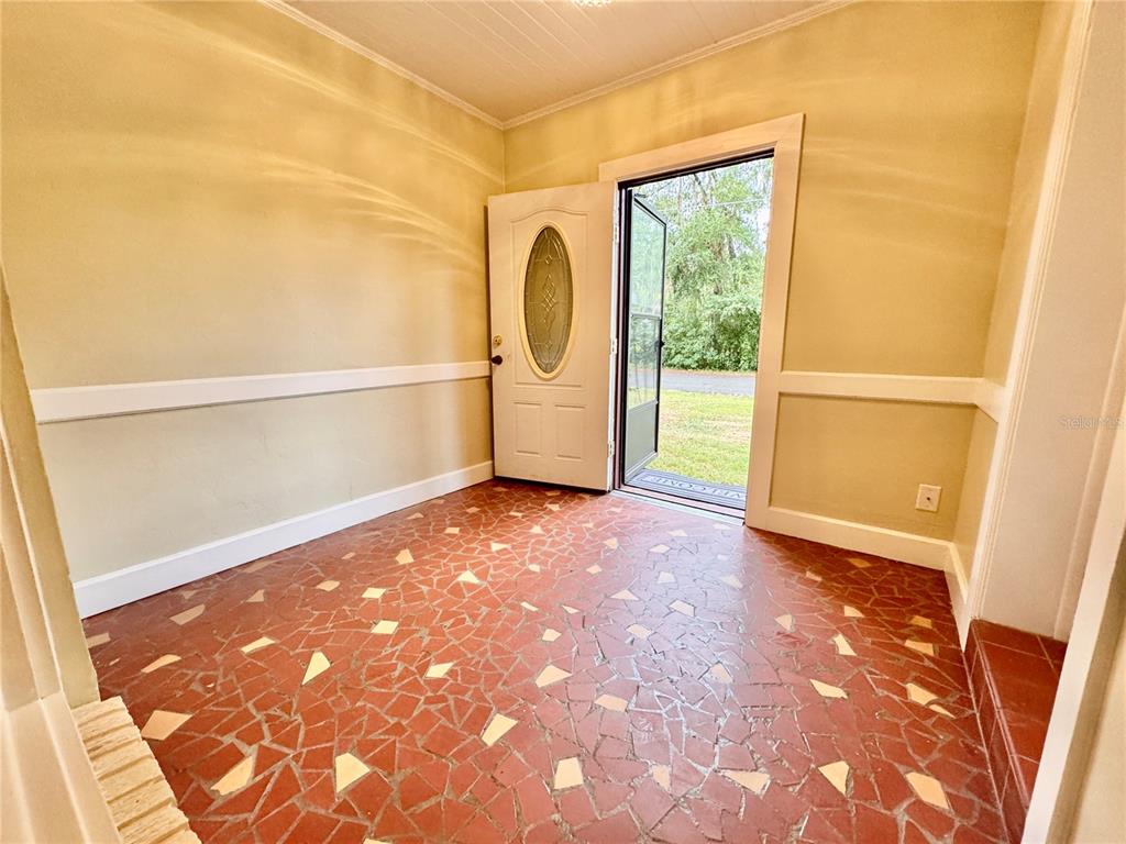 An entryway features a red flagstone floor, beige walls with wainscoting, and an open front door — 905 NW 36TH AVENUE, GAINESVILLE, FL