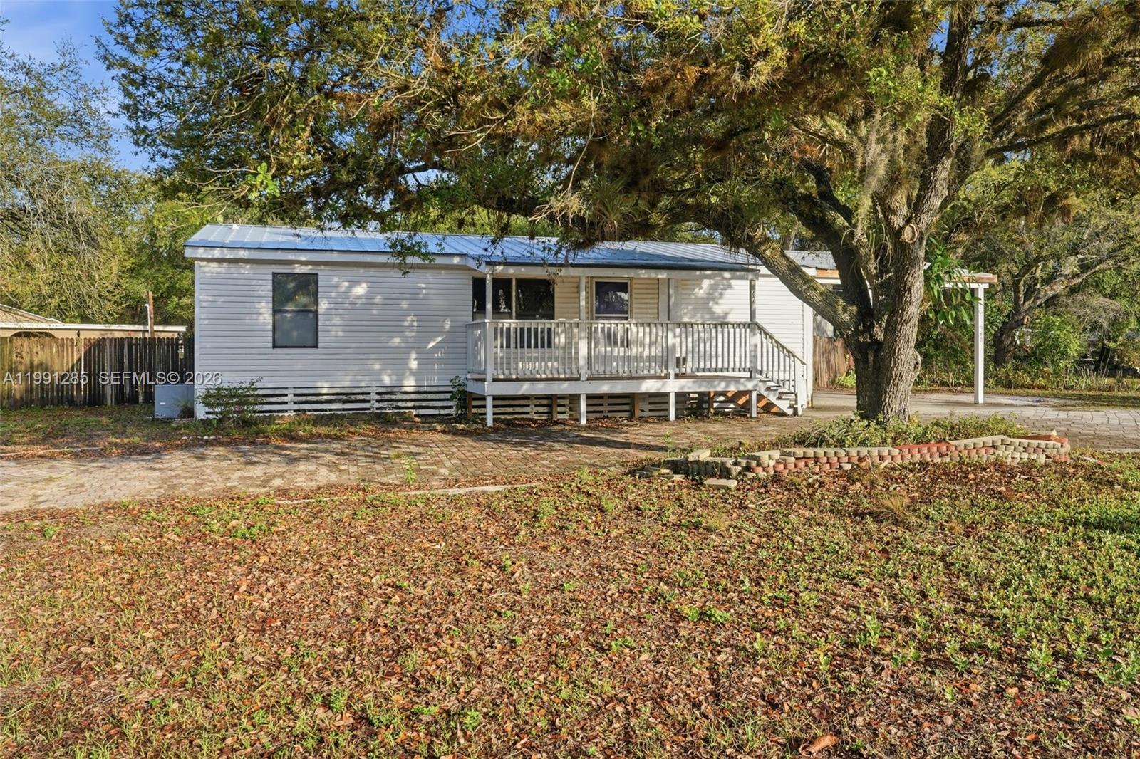 A white single-story house with a front porch sits under a large oak tree — 740 bennett ave, La Belle FL 33935, LA BELLE, FL