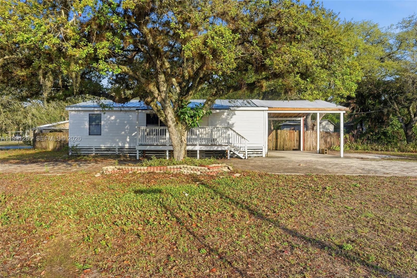 A white single-story house with a front deck and attached carport under a large tree — 740 bennett ave, La Belle FL 33935, LA BELLE, FL