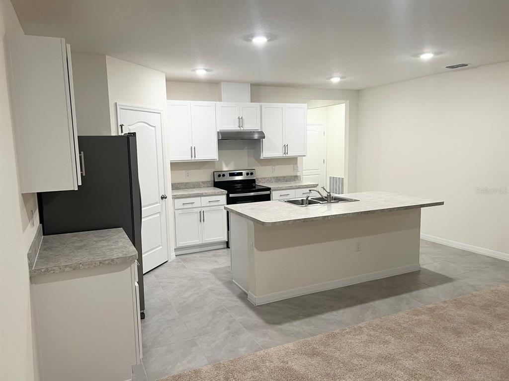 A kitchen features white cabinets, gray countertops, a center island, and light-colored tile flooring — 709 VERSAILLES LANE, KISSIMMEE, FL