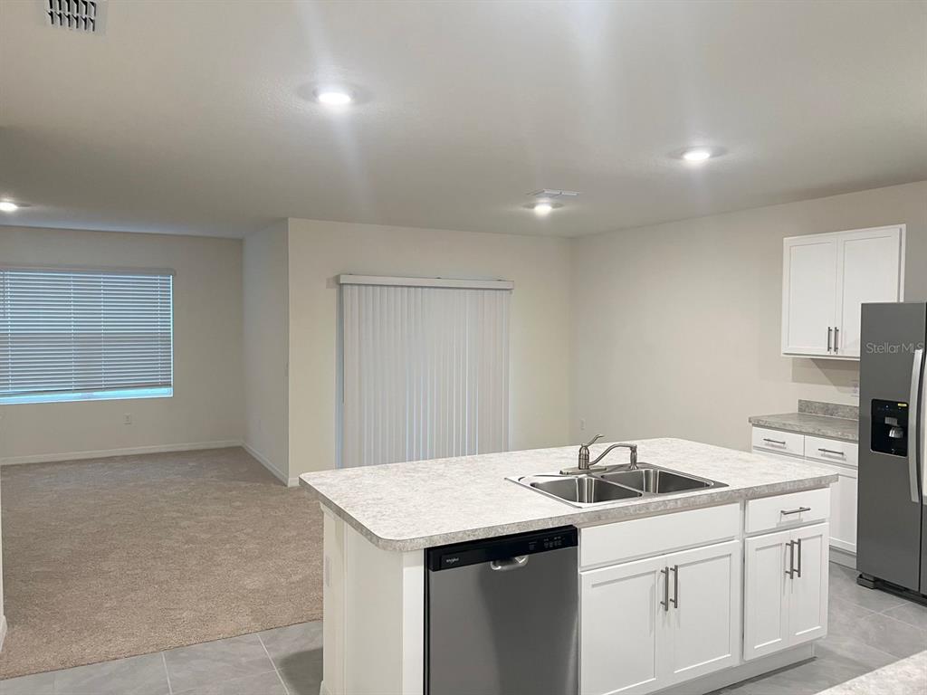 A kitchen island with a stainless steel dishwasher faces a living area with carpeted flooring — 709 VERSAILLES LANE, KISSIMMEE, FL