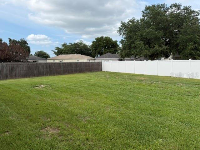 A large, grassy backyard is enclosed by a combination of wood and white vinyl fencing — 709 VERSAILLES LANE, KISSIMMEE, FL
