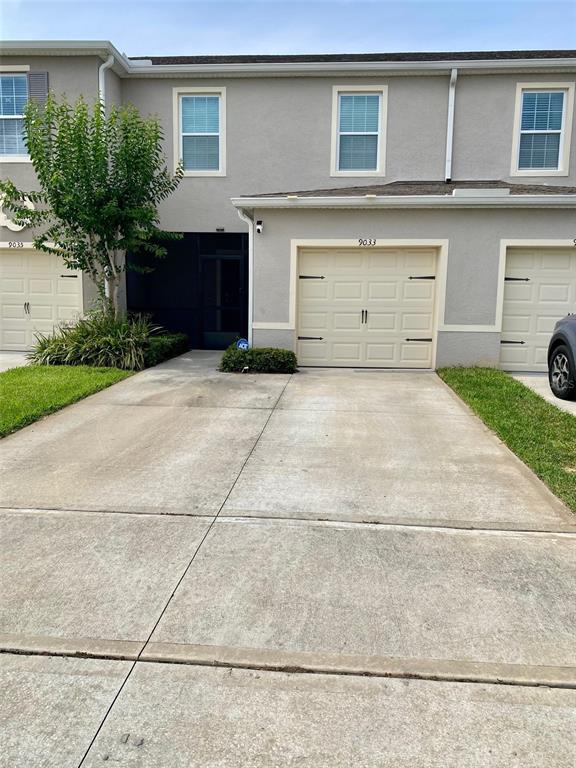 A two-story townhouse exterior features a concrete driveway, a single-car garage, and a small tree — 9033 ALBA LANE, KISSIMMEE, FL