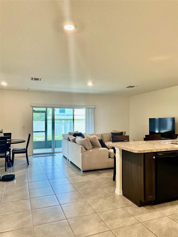 An open-concept living room and kitchen area features tile flooring and a sliding glass door — 9033 ALBA LANE, KISSIMMEE, FL