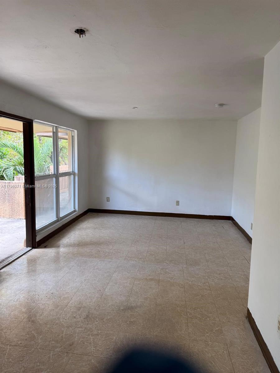 An empty room features beige tile flooring, white walls, dark baseboards, and a sliding glass door — 1600 NW 4th Ave # 16A, Miami FL 33136, MIAMI, FL