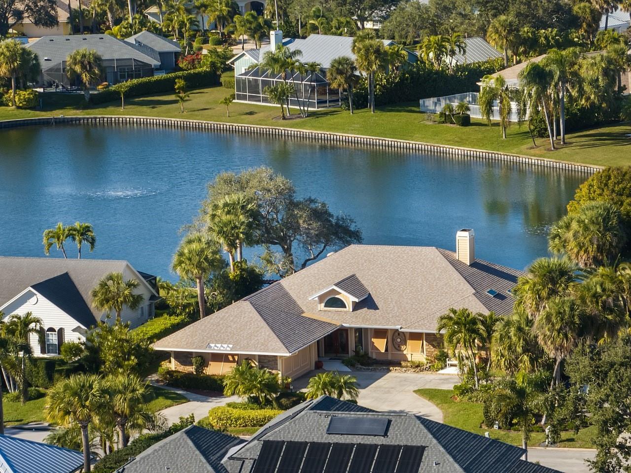 An aerial view shows several houses with shingled roofs situated around a large, curved lake — 72 Cache Cay Drive, Vero Beach FL 32963, VERO BEACH, FL