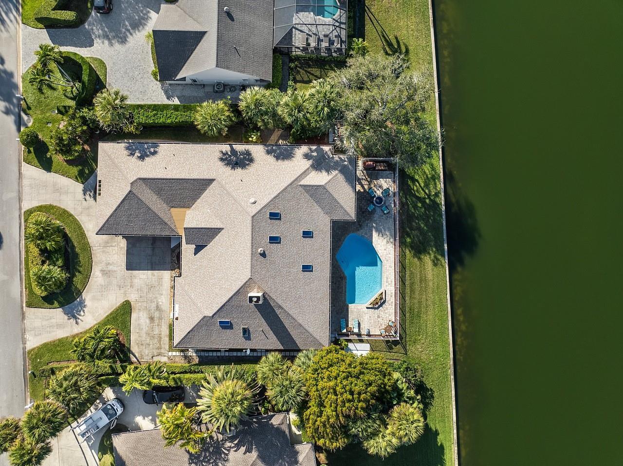 An aerial view shows a house with a swimming pool and patio beside a lake — 72 Cache Cay Drive, Vero Beach FL 32963, VERO BEACH, FL