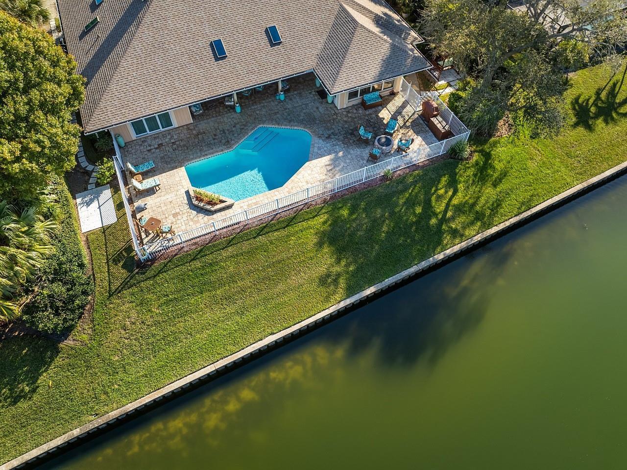 An aerial view of a house with a pool, patio, and lawn bordering a canal — 72 Cache Cay Drive, Vero Beach FL 32963, VERO BEACH, FL
