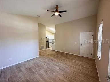 An open-concept living room with wood-look tile flooring, a ceiling fan, and an adjacent kitchen — 21915 BELL LAKE ROAD UNIT 2, LAND O LAKES, FL