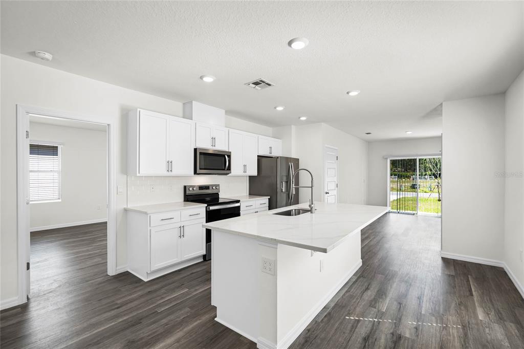 A modern kitchen features white cabinets, a marble-topped island, and dark wood-look flooring — 1746 HUMMINGBIRD ROAD, WINTER HAVEN, FL