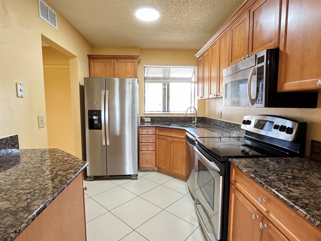 A kitchen features wooden cabinets, granite countertops, stainless steel appliances, and light-colored tile flooring — 2017 SKIMMER CT W UNIT 424, CLEARWATER, FL