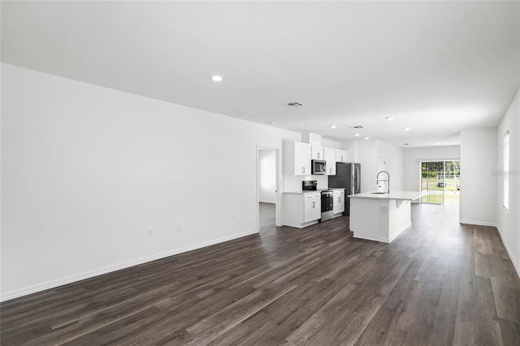 An open-concept kitchen and living area with white cabinets, an island, and wood-look flooring — 1660 HUMMINGBIRD ROAD, WINTER HAVEN, FL