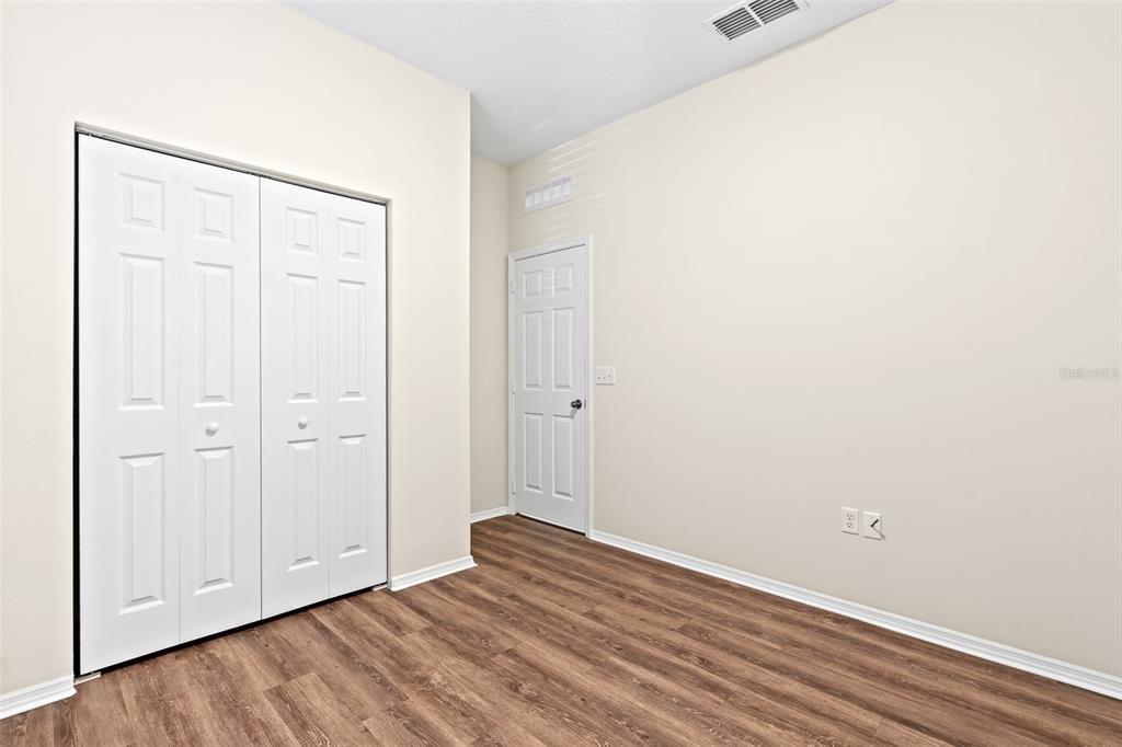 An empty room features wood-look flooring, a white closet with bifold doors, and a door — 535 AEOLIAN DRIVE, NEW SMYRNA BEACH, FL