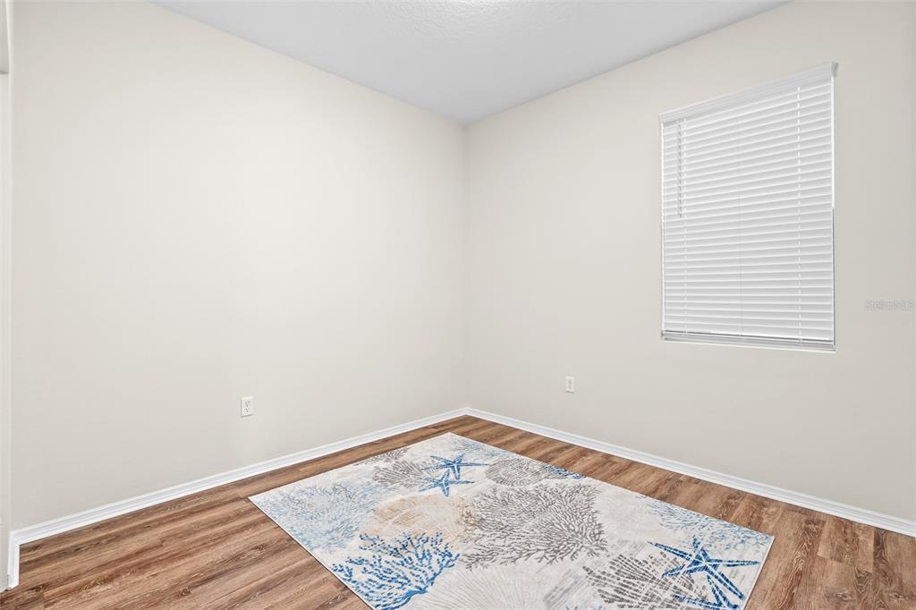 An empty room with light-colored walls, wood-look flooring, a window with blinds, and a rug — 535 AEOLIAN DRIVE, NEW SMYRNA BEACH, FL