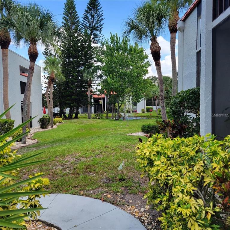 A grassy courtyard sits between two apartment buildings with palm trees and a small pond — 3275 BENEVA ROAD UNIT 104, SARASOTA, FL