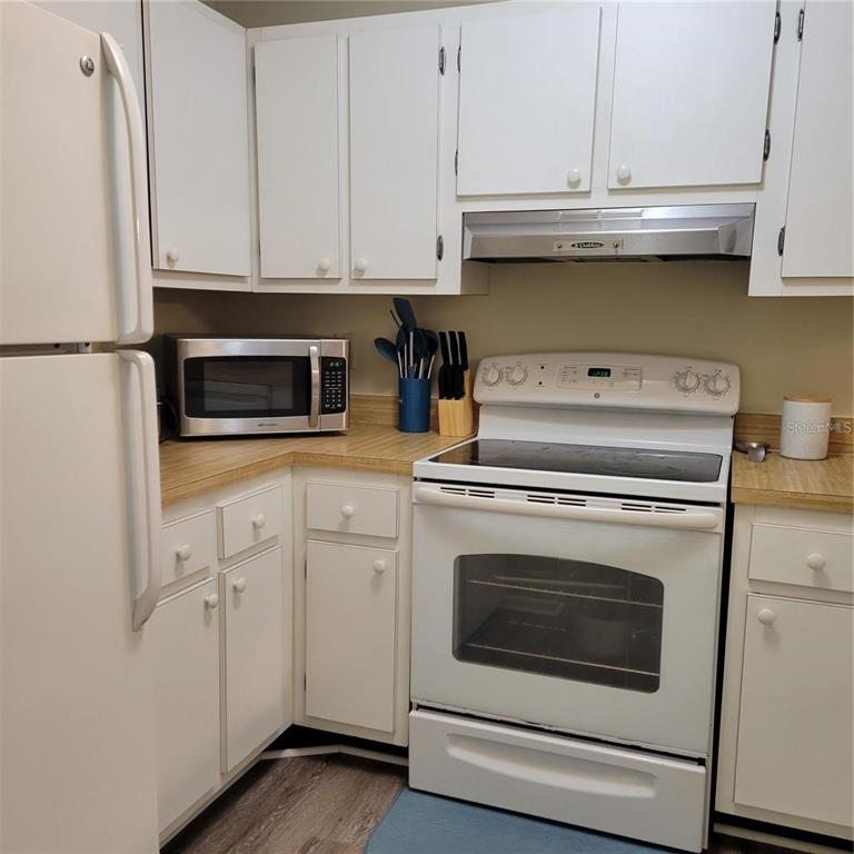 A kitchen features white cabinets, a white stove, a microwave, and light-colored laminate countertops — 3275 BENEVA ROAD UNIT 104, SARASOTA, FL