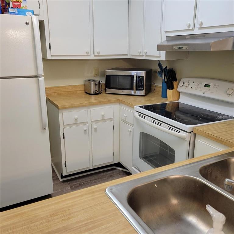 A kitchen features white cabinets, laminate countertops, a white refrigerator, and a stainless steel microwave — 3275 BENEVA ROAD UNIT 104, SARASOTA, FL