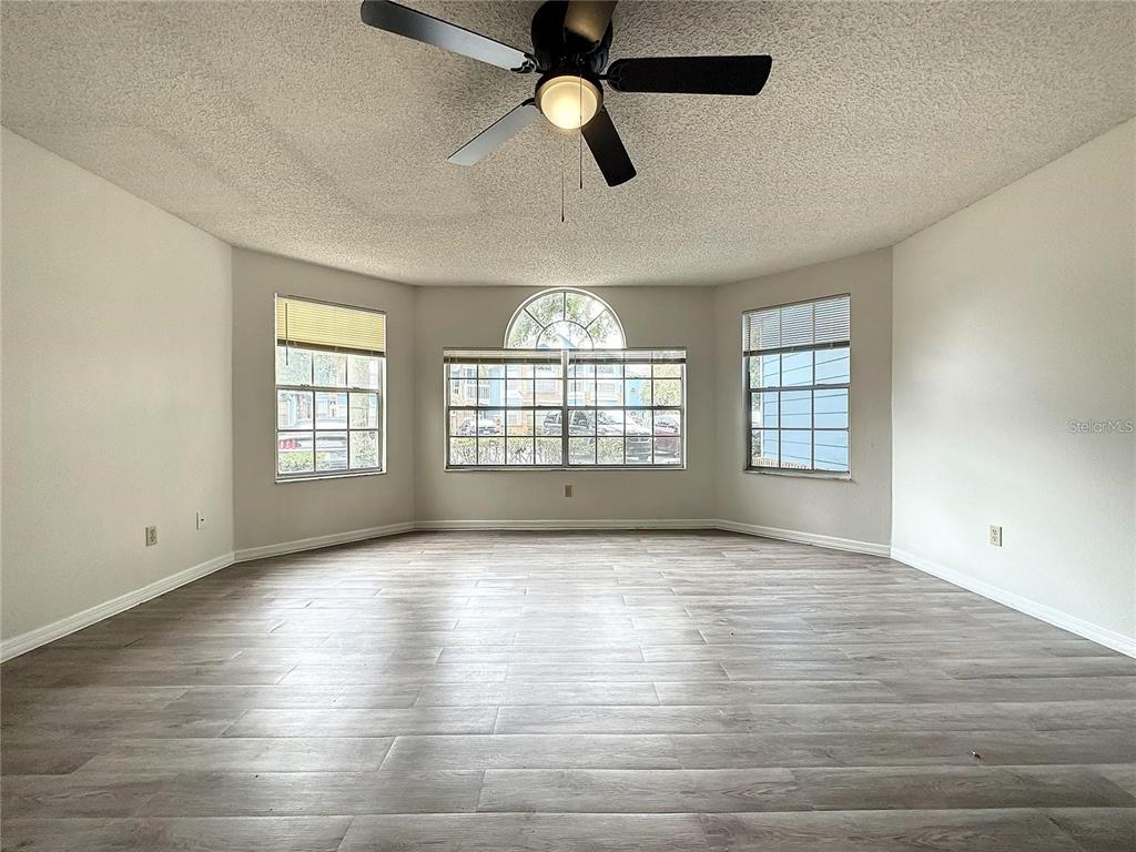 An empty room features light wood-look flooring, white walls, a ceiling fan, and large windows — 2717 N POINCIANA BLVD UNIT 173, KISSIMMEE, FL