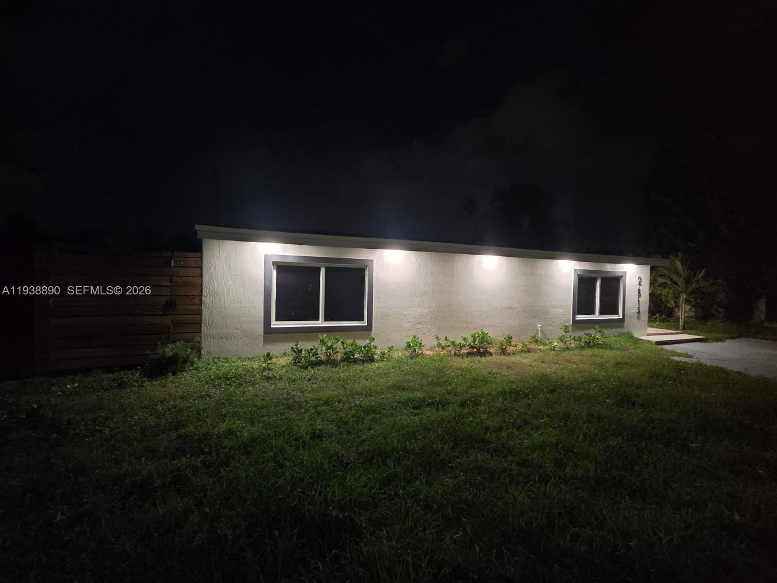 The exterior of a single-story house at night features recessed lighting and two windows — 2615 NW 62nd Ave, Margate FL 33063, MARGATE, FL