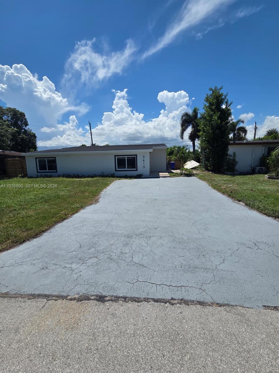 A single-story house with a gray driveway and a large lawn under a cloudy sky — 2615 NW 62nd Ave, Margate FL 33063, MARGATE, FL
