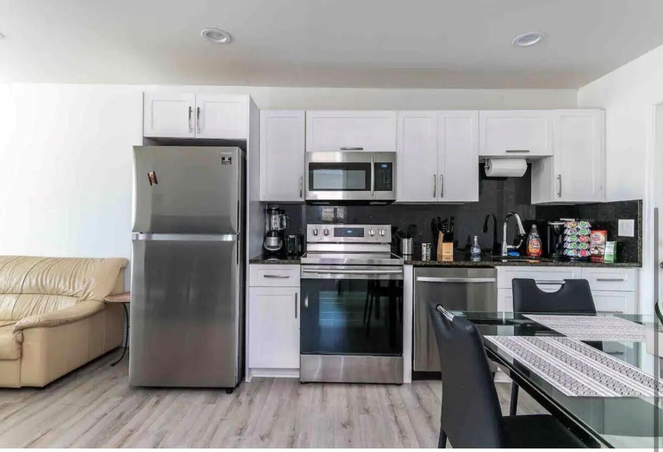 A kitchen features white cabinets, stainless steel appliances, and dark countertops next to a sofa — 2499 NE 2nd Avenue # B, Boca Raton FL 33431, BOCA RATON, FL