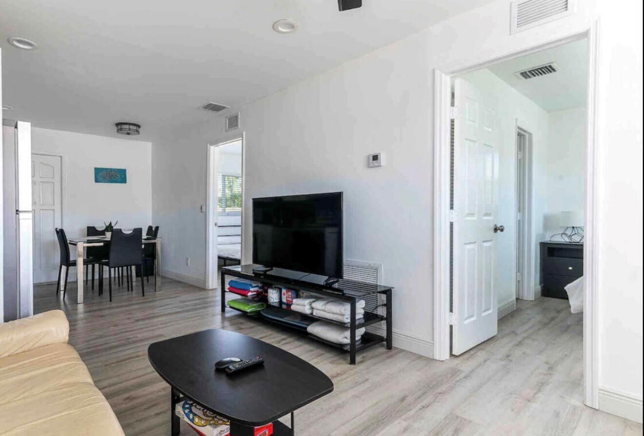 A living room with light wood-look flooring, a television on a stand, and a dining area — 2499 NE 2nd Avenue # B, Boca Raton FL 33431, BOCA RATON, FL