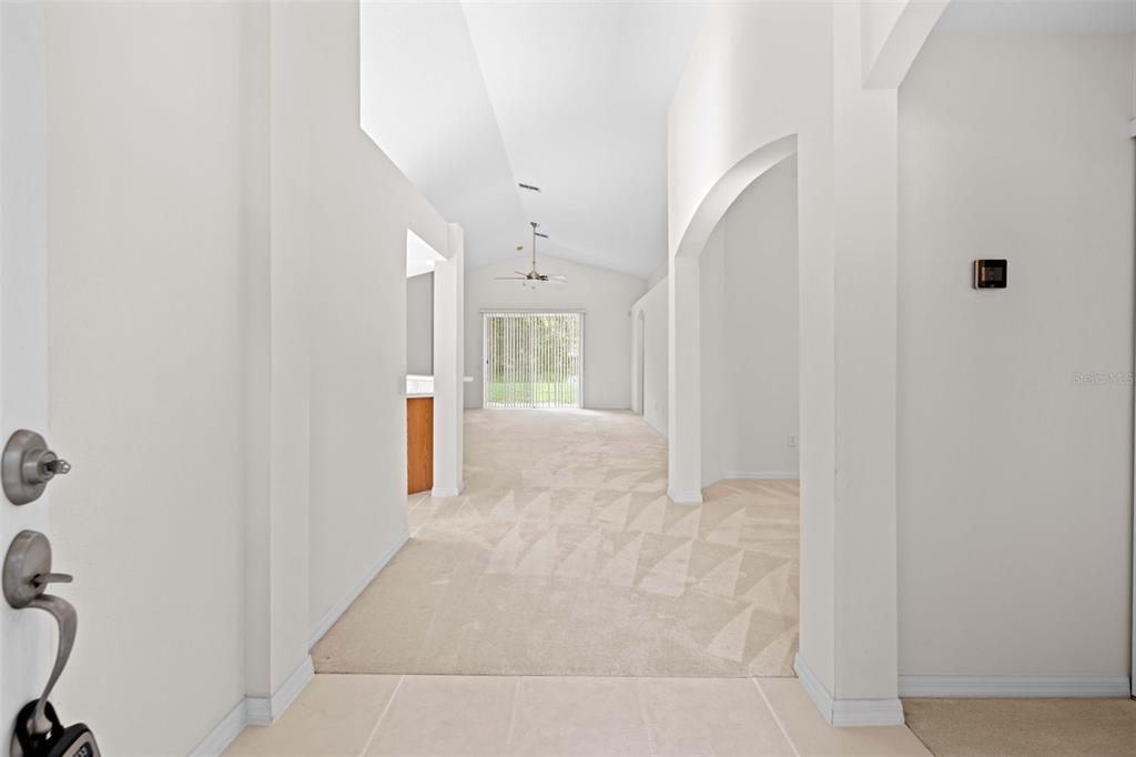 An entryway leads into a living area with vaulted ceilings, carpeted floors, and sliding glass doors — 13233 BAINBRIDGE WAY, SPRING HILL, FL