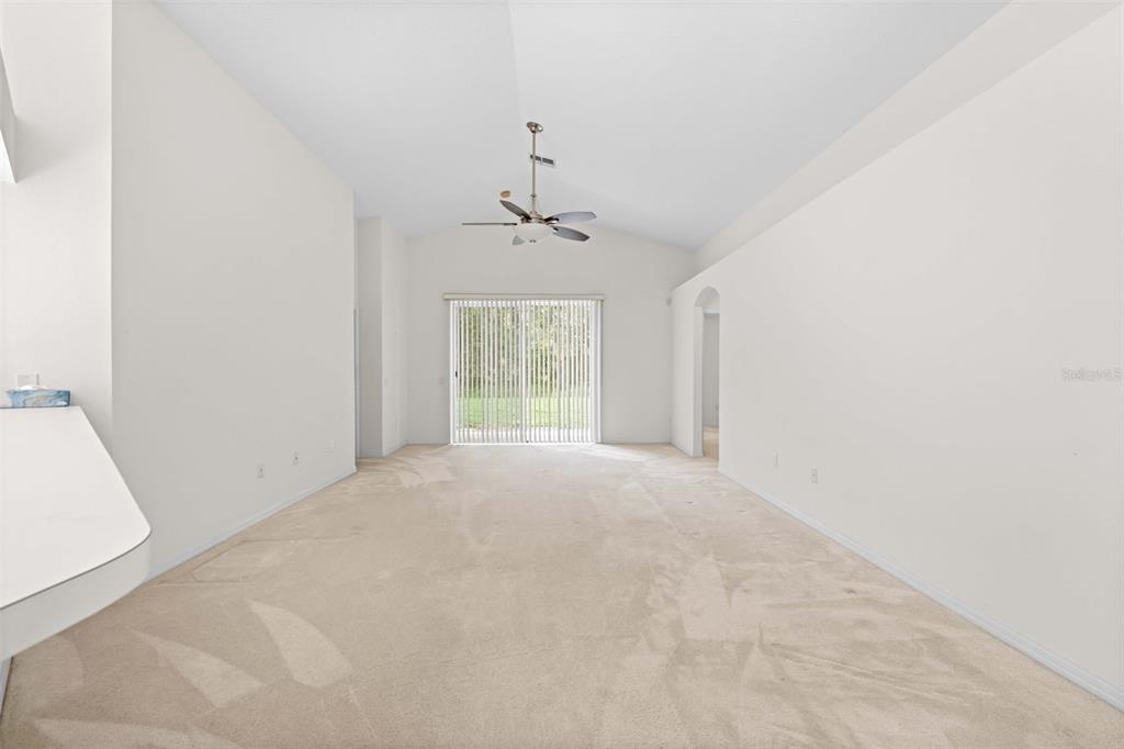 A spacious, carpeted living room features white walls, a ceiling fan, and sliding glass doors — 13233 BAINBRIDGE WAY, SPRING HILL, FL