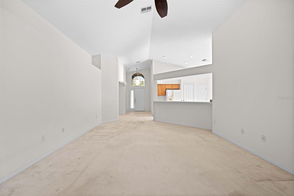 A spacious living room with beige carpet, vaulted ceilings, and a pass-through to the kitchen — 13233 BAINBRIDGE WAY, SPRING HILL, FL